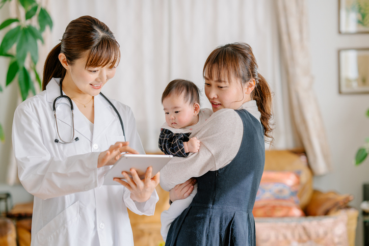 Photo shows a pediatrician visiting a young mum and her infant baby daughter in the living room at home/Getty Images