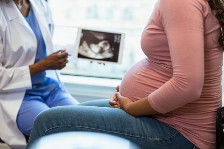 Photo shows a doctor speaking to a pregnant patient with an ultrasound image in the background/Getty Images