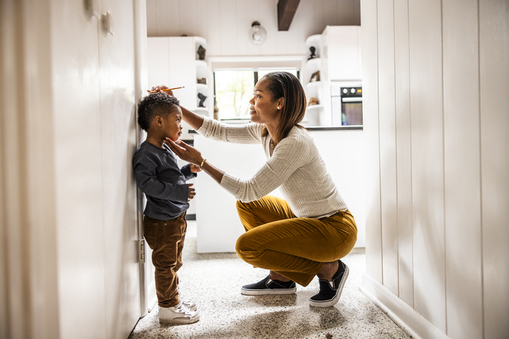 Photo shows a mother measuring son's height on wall in kitchen/Getty Images